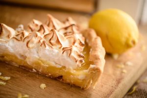 Slice of lemon meringue pie on wooden cutting board